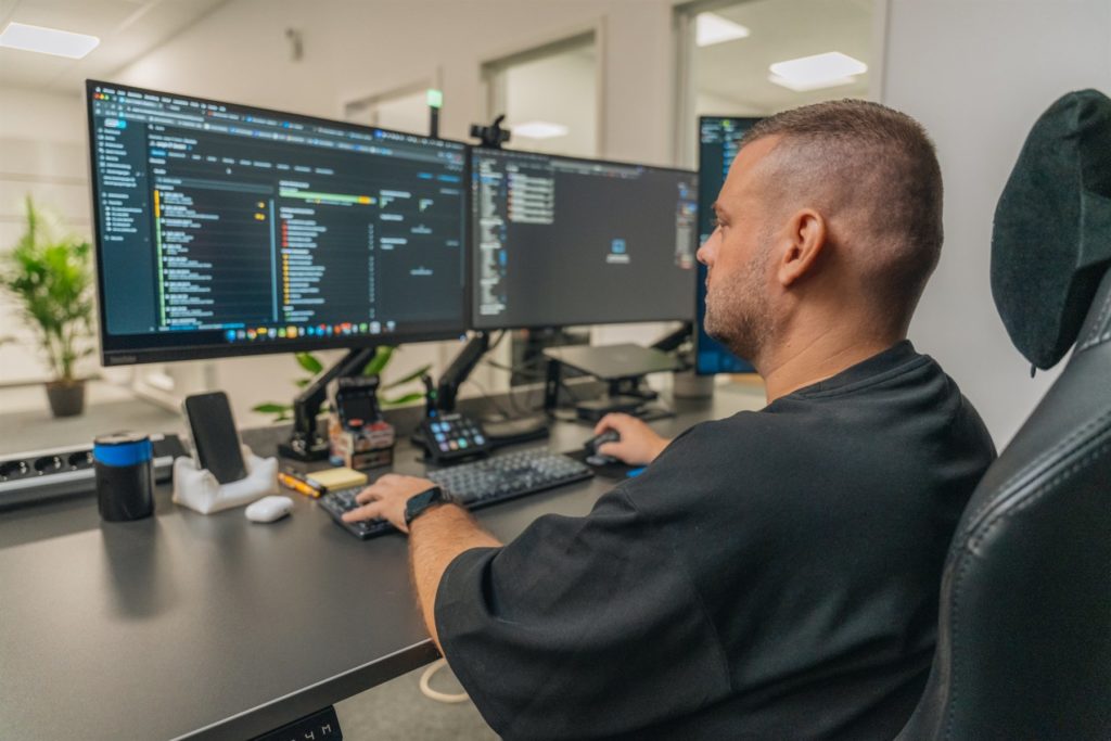 Kollege arbeitet konzentriert an drei Monitoren im Büro