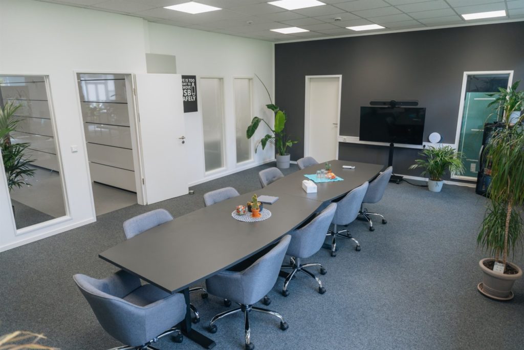 Besprechungsraum mit langem Tisch, Bildschirm und Pflanzen