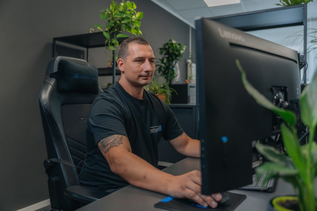 Kollege am Arbeitsplatz zwischen Bildschirm und Pflanze