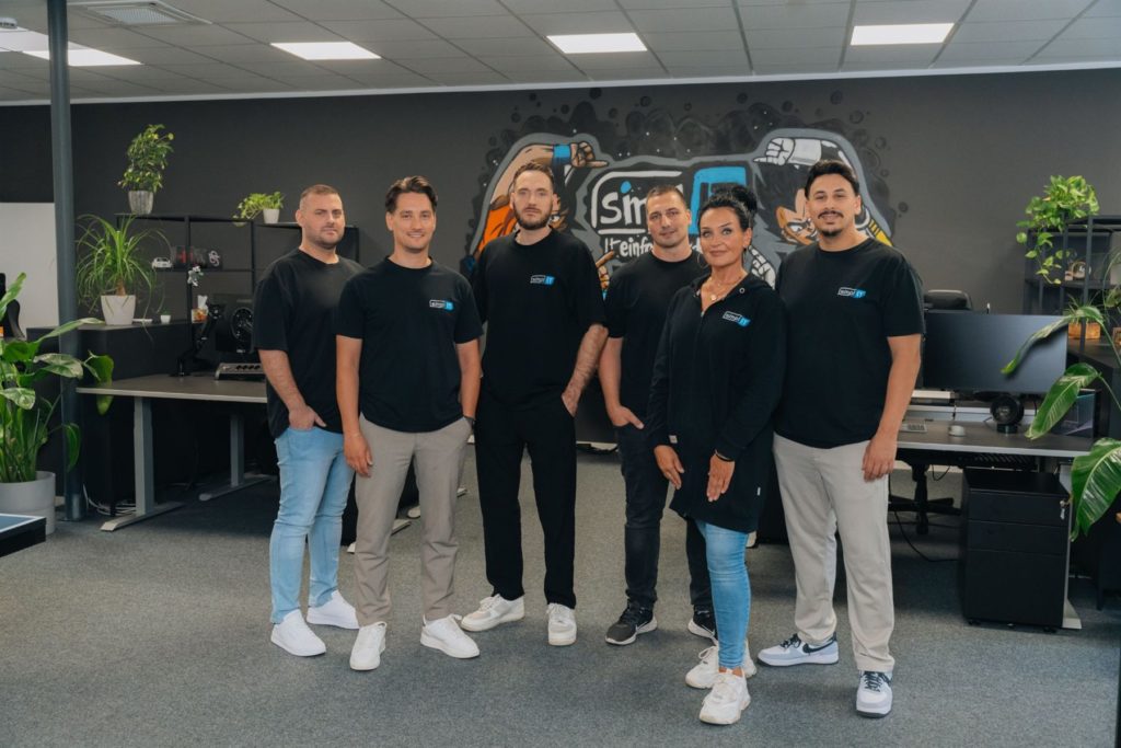 Das smpl-IT Team steht gemeinsam im Büro vor dem Wandgemälde